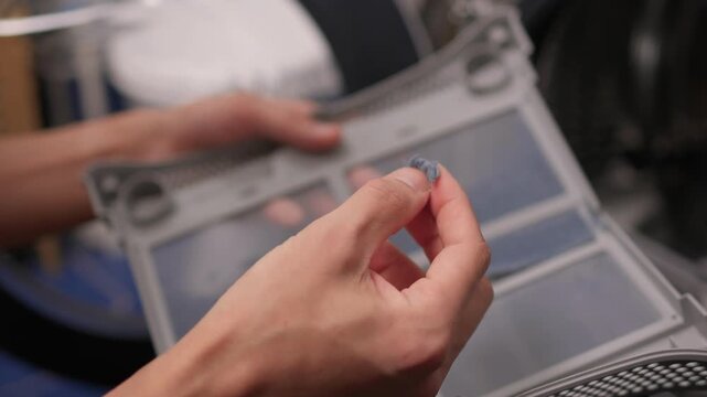 Hands pulling grey lint from dryer filter, removing heavy debris clumps, closeup of fingers collecting fibers, messy cleanup and satisfying disposal, home maintenance demonstration