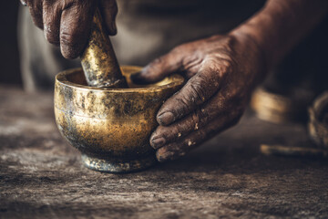 Vintage brass mortar and pestle held by aged hands on rustic wooden table showing traditional tool for grinding with textured surface and warm nostalgic atmosphere