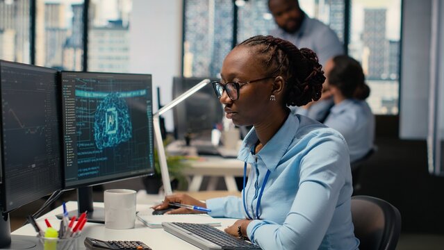 Trader in office leverages AI technology on PC to interpret analytics charts, optimizing buying and selling. African american woman uses deep learning automatization to maximize profits