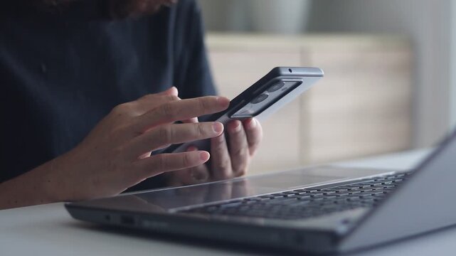 Woman hands using mobile phone while working at laptop. Female fingers typing and tapping on smartphone. Texting and scrolling to check email or text SMS message. Online business communication concept