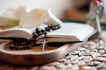 Rosary beads and open Catholic Bible on wooden tray