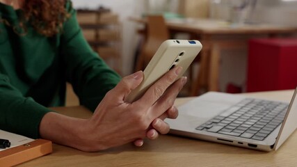 Close up of female hands using smartphone and laptop at desk. Remote freelance work and online communication in home office. Technology and connectivity concept. - Powered by Adobe