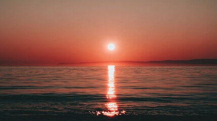 Brilliant solar orb descends below the horizon casting strong reflection across placid ocean water