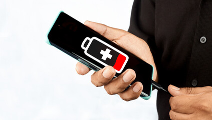 A hand holding a smartphone displaying a low battery warning while being charged, illustrating power shortage, device dependency and urgent energy recovery.
