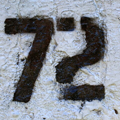 Weathered number 73 painted on cracked white wall