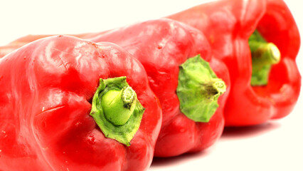 Fresh red bell peppers with green stems on white.