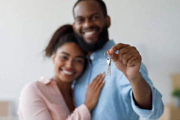 Smiling young afro american couple hugging and show keys to new property at home interior. Happy owners express positive emotions from buying new apartment, family moving to new house, free space