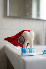 Superhero tooth model standing on a toothbrush with a cape, showcasing dental hygiene, on a bathroom countertop, viewed from the side.