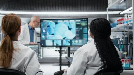 Senior scientist presenting new drug development findings to pharmaceutical team in lab. Expert pointing at large screen displaying cellular reaction during training meeting, camera A