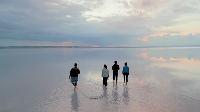 Friends walking barefoot with a dog on the salt flat reflecting the cloudy sky at sunset drone aerial view in Turkey