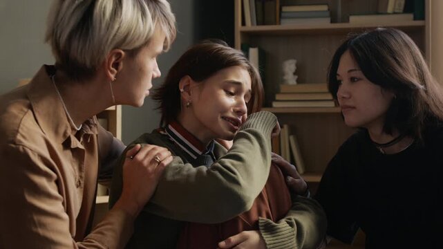 Adult female psychologist comforting tearful teenage girl while empathetic group members listening during therapy session