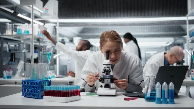 Histology technician examining pathology slides under microscope in research center. Female researcher driving medical innovation through dedicated cellular analysis work, camera A