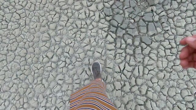 Woman walking over a vast landscape of cracked dry earth symbolizing drought and environmental crisis