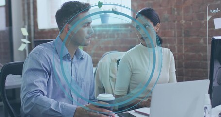 Discussing coworkers in business casual working at desk in office, laptop and blue AR overlay