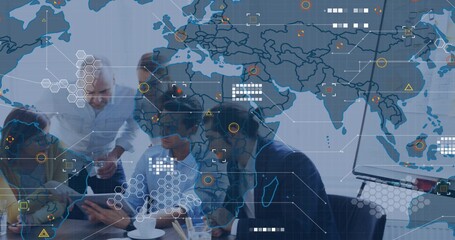 Collaborating team of five in suits reviewing tablet, laptop at office table with map overlays