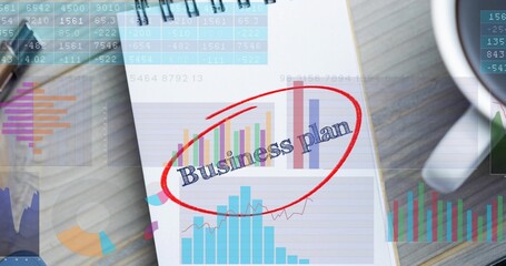 Displaying spiral-bound notepad showing Business plan red-circled with printed charts on wood desk