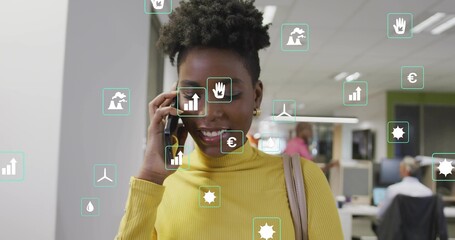 Holding smartphone to ear, woman in yellow turtleneck talking in open office, showing green icons