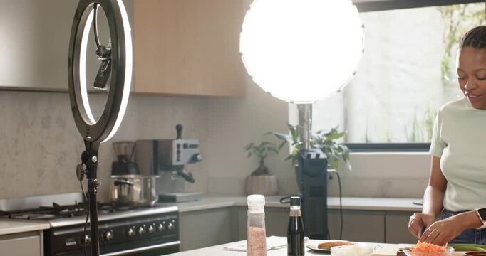 African American women chopping on kitchen island under ring light, seasoning and tasting for demo