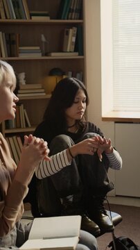 Vertical shot of black haired teenage girl staying emotionally distant while adult female therapist speaking to adolescents during group discussion in psychotherapy session