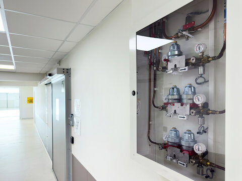 Lyon, France - Jun 9, 2025: Medical hallway with a secured wall cabinet displaying pressure gauges and gas regulators for hospital systems next to a closed automatic door in a clean corridor