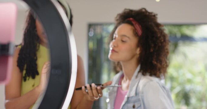 Ring light shifting revealing diverse female friends teaching makeup brush technique near window