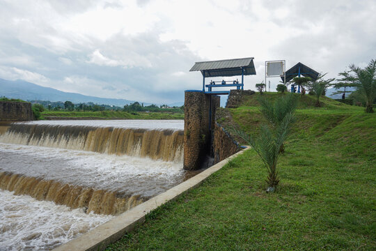 The brownish river water flows rapidly from an irrigation system and a small dam as a means of controlling the water of the rice fields
