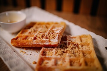 Sweet waffles topped with powdered sugar and nut crumbs served on a white plate. Cozy homemade...