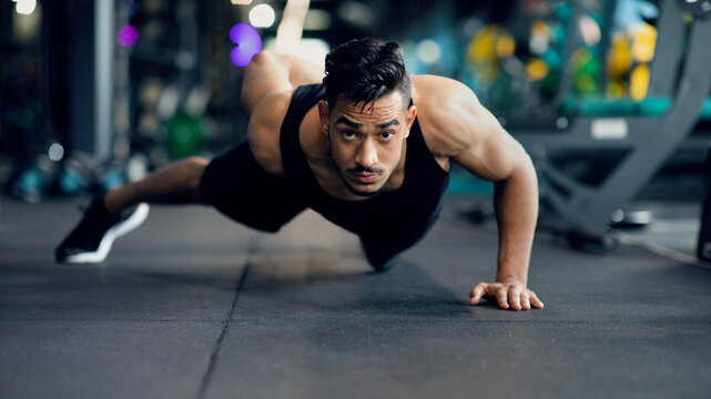 Motivated Young Arab Sportsman Making Push Up Exercise On One Hand, Portrait Of Handsome Muscular Middle Eastern Male Athlete Training In Modern Gym Interior, Doing Bodybuilding Workout, Panorama