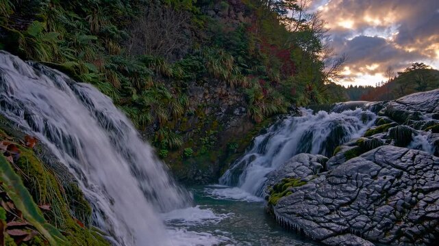 A stunning wide-angle video capture of a cascading waterfall at sunset, highlighting lush greenery and dramatic skies in a serene natural setting.
