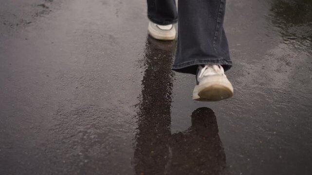 white sneaker walking on wet pavement, closeup of single step with puddle reflection, denim hem, scuffed sole, muted overcast lighting, glossy asphalt texture, gentle splash and steady rhythm