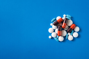 Assorted medical pills and capsules on blue background with copy space