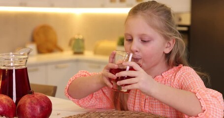Little girl drinking fresh pomegranate juice at table indoors