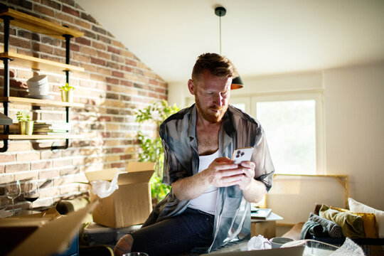 Man using smartphone while unpacking boxes in home kitchen