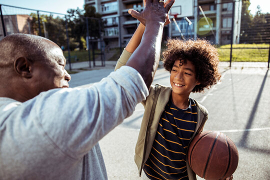 Man and boy high-five during basketball practice at outdoor court