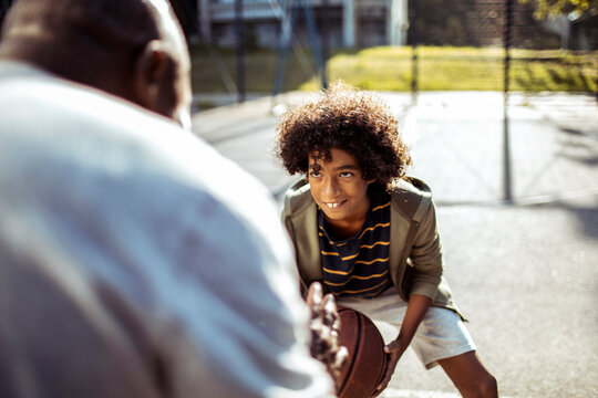 Smiling boy dribbling basketball with adult on outdoor court