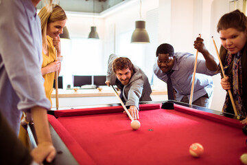 Coworkers playing billiards in modern office breakroom