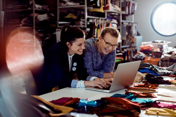 Two fashion designers collaborating on a laptop in a fabric studio