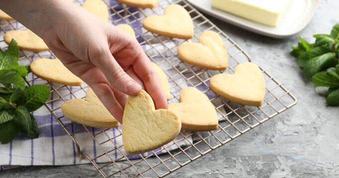 Woman taking tasty heart shaped butter cookie from cooling rack at grey textured table, closeup