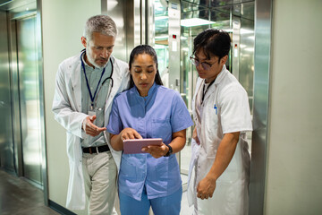 Doctors and nurse reviewing patient records on tablet in hospital corridor