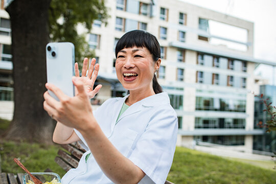 Smiling nurse video calling on smartphone outside hospital