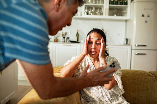 Stressed couple reacting to smartphone news in home kitchen