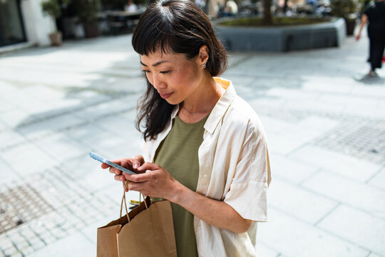 Woman checking smartphone with shopping bags in city