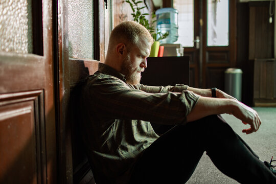 Depressed bearded man sitting on office floor