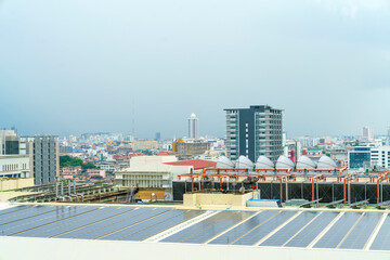 Solar panels installed on a city rooftop with industrial HVAC systems and a dense urban skyline background. Sustainable energy and modern infrastructure in a metropolitan area under a cloudy sky.