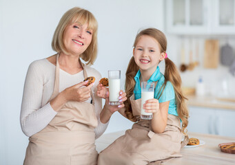 Snack Time. Portrait of happy granny and little girl enjoying homemade pastry and drinking milk in...