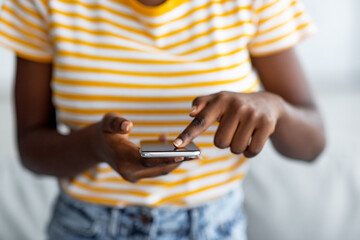 Unrecognizable black woman in casual using brand new mobile phone at home, touching screen with finger, unlocking device, closeup. Finger identification for modern gadgets, security, id concept