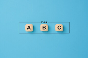 Plan a, b and c on wooden cubes on blue background. Choosing a business strategy plan out of three options