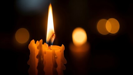Close up of a lit candle with a flickering flame and bokeh background.