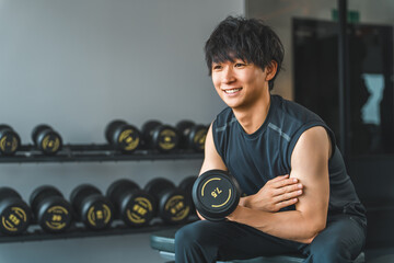 Young Asian man doing dumbbell training at fitness gym