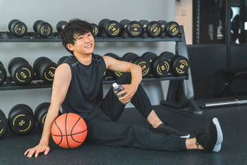 Young Asian man holding basketball and weight ball in gym